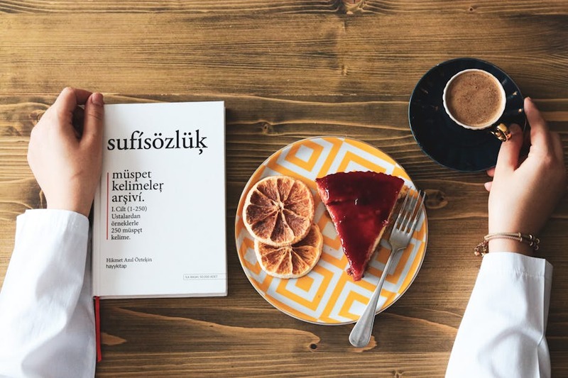 A top view of coffee, cake, and a book on a wooden table, creating a cozy breakfast scene.