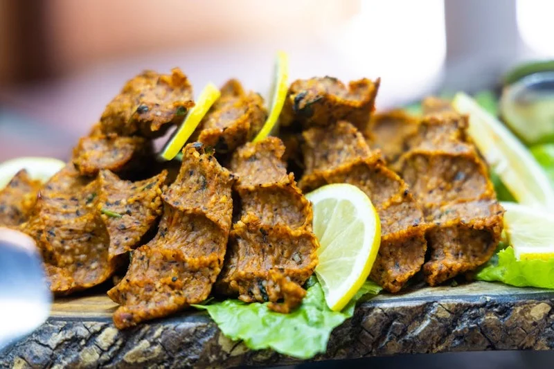 Taze yeşillikler ve limonla servis edilen Türk vegan mercimek köftesi tabağı